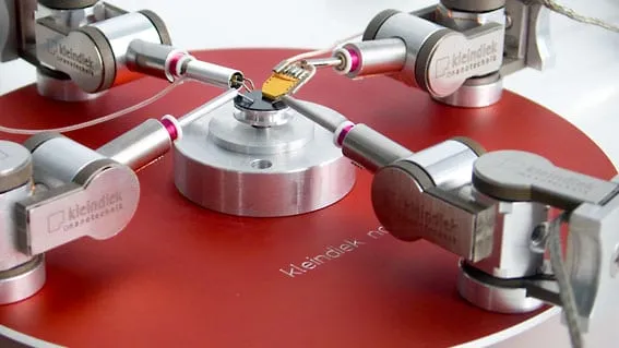 An MM3A-LMP probe station with four manipulators converging on a chip mounted at the centre of a red rotating stage.