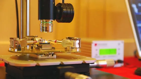 A wide view of an MM3A-LMP probe station under a light microscope, with manipulators and a readout unit on the bench.