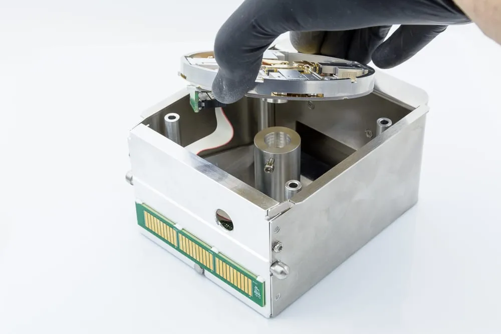 Top-down view into the assembled shuttle showing four probe assemblies wired across a gold-plated circular contact disc around the central sample position.