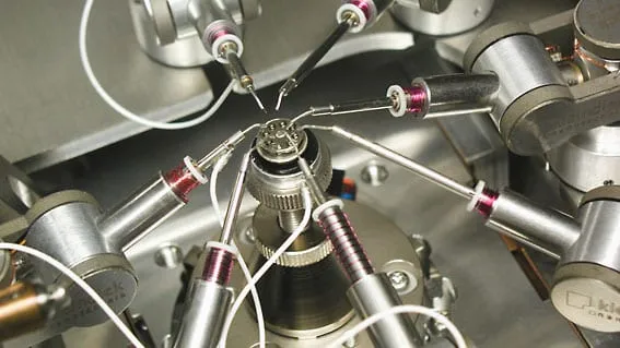 Photograph of a multi-arm nanoprobe station inside a chamber, several probe holders converging on a central sample stage, each wired with a shielded cable.