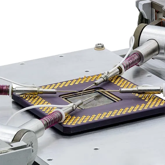 Angled view of four MM3A-EM micromanipulators probing an opened device package on the NW4 platform.