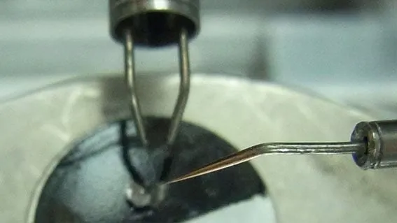 Close-up inside the chamber of the MSU tip approaching a small wire loop clamped in a sample mount.
