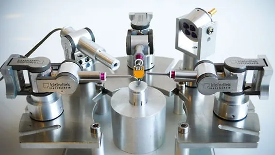 An in-chamber view of two Kleindiek micromanipulators flanking a central sample pillar, with the SemCam camera module viewing from the upper right.